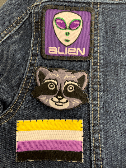 pride flag, raccoon, and alien badges on a jacket